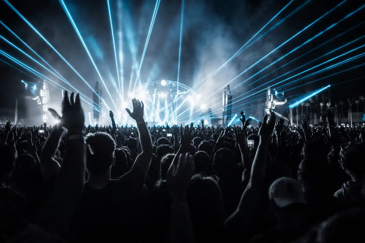 A crowd with hands raised beneath blue concert lights